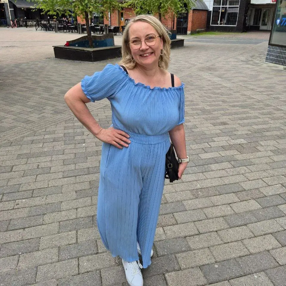 Susanna seisoo hymyillen torilla vaaleansinisessä haalarissa, käsi lantiolla.